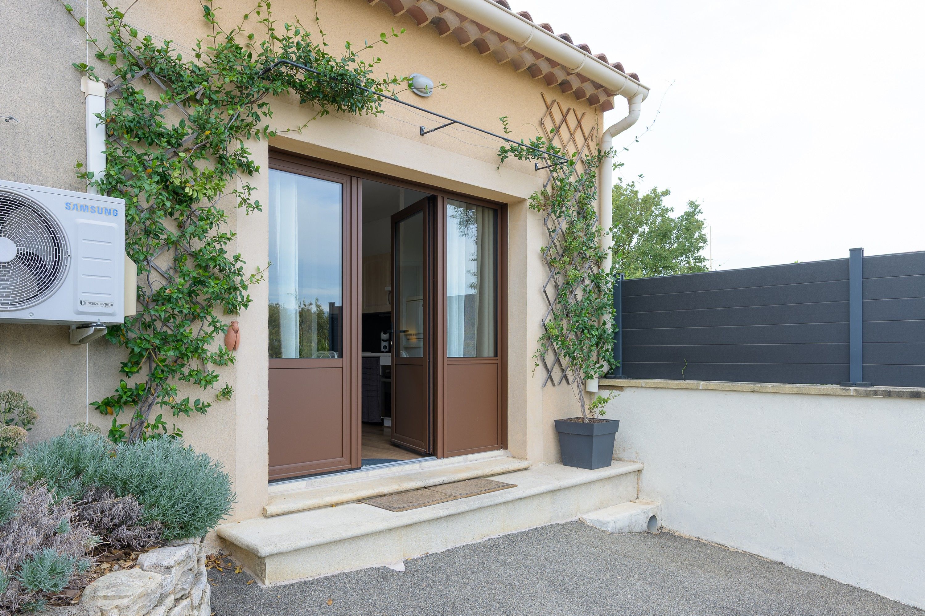 Un immeuble résidentiel avec une porte marron, un grand climatiseur et un pot de fleurs.