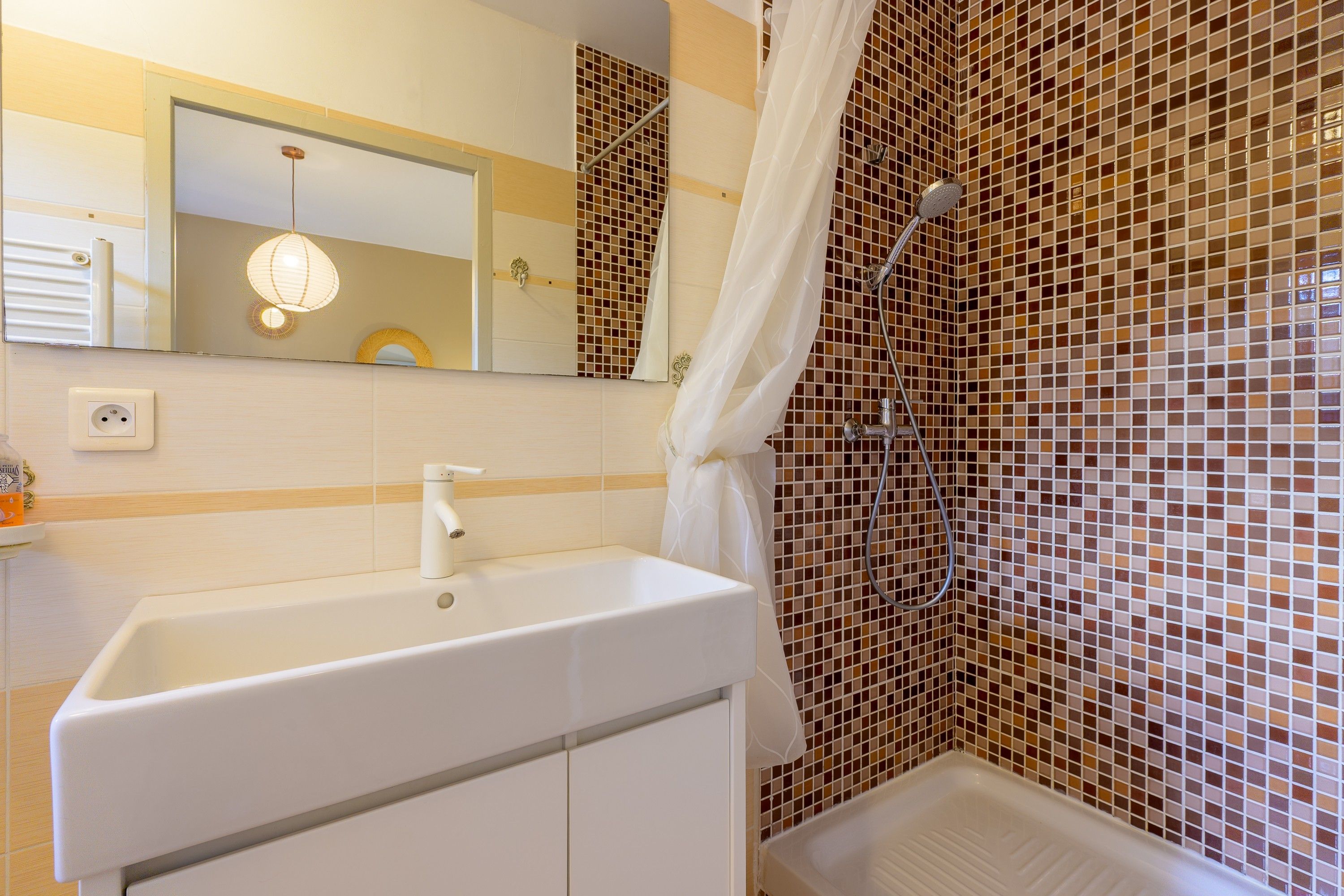 A bathroom with a white sink, a shower with a glass door, and a tiled wall.
