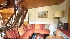 A cozy living room with a wooden staircase, a sectional sofa, a coffee table, and a painting on the wall.