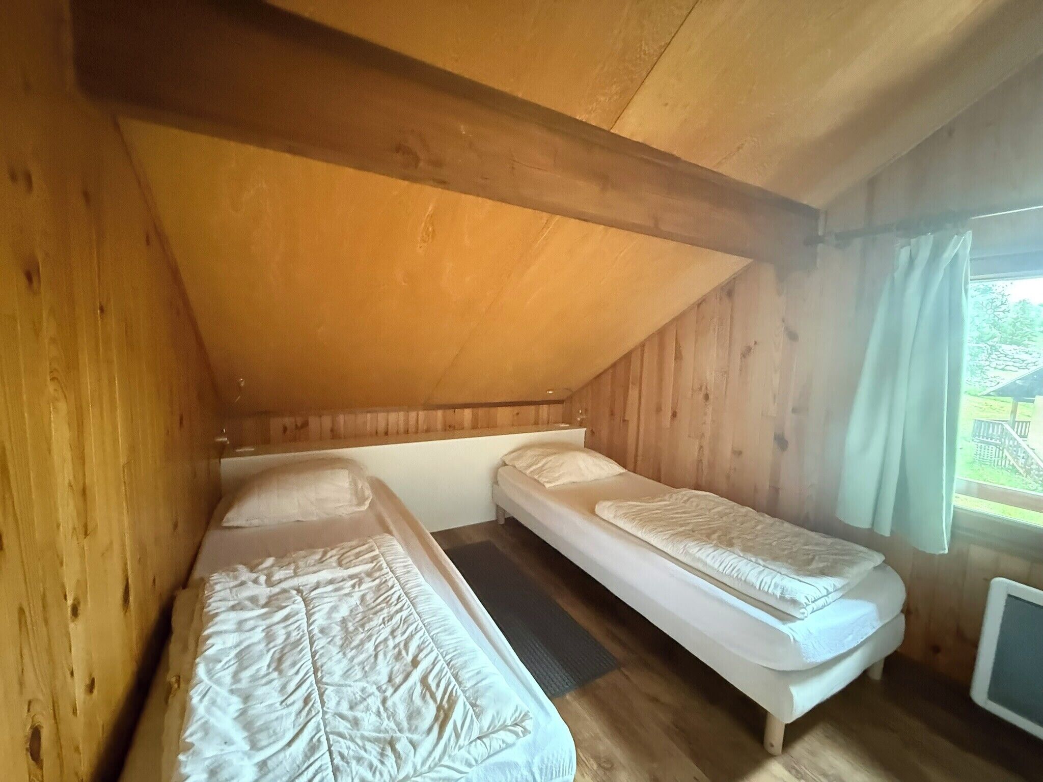 A small, wooden cabin room with two single beds, a window with curtains, and a television on the right.