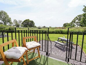 A wooden bench with a cushion, a picnic table, and a metal fence in a park setting. - Quackin' Up (Whitchurch)