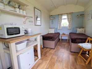 A compact room with a kitchenette, two beds, a small table, and a window with curtains. - Quackin' Up (Whitchurch)