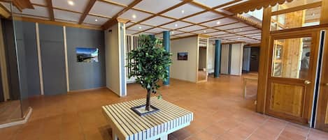 A spacious lobby with a tiled floor, a wooden bench with a potted plant, and a wooden door on the right.