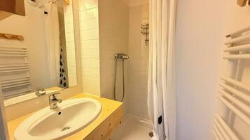 A bathroom with a sink, mirror, shower, and towel rack.