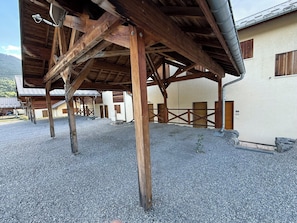 A building with a gravel courtyard, wooden beams, and a metal roof. - Chalet cosy à Risoul village • Terrasse & vue vallée (Risoul)