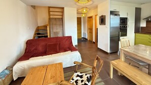 En moderne stue med sofa, spisebord og et køkkenområde med køleskab og mikroovn.