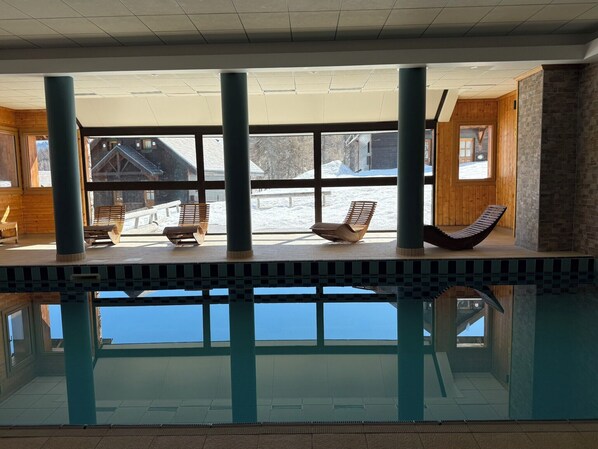An indoor swimming pool with clear views of a snowy landscape through large windows.