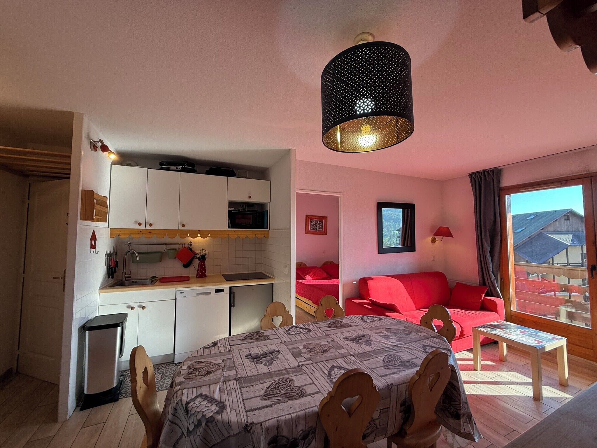 A compact living space with a kitchenette, a dining table, a red sofa, and a large window.