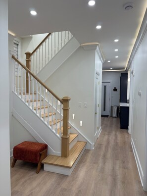 A staircase with wooden balusters and a red bench, leading to a hallway with recessed ceiling lights and a trash can.