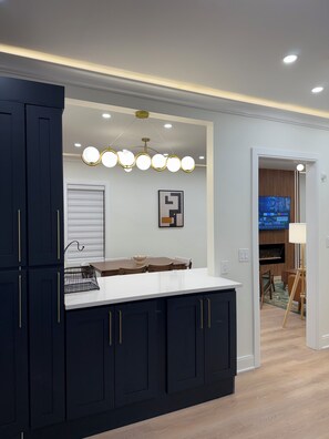 A modern kitchen with dark cabinetry, a white countertop, and a unique pendant light fixture.