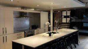 A modern kitchen with a central island, bar stools, and a staircase leading to a loft area. - Smith's Irish Pub & Accomodation (Vancouver)