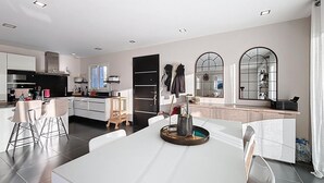 Eine moderne Küche mit weißen Schränken, ein Essbereich mit einem weißen Tisch und ein großer Spiegel.