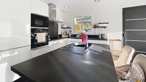 Eine moderne Küche mit weißen Schränken, einer schwarzen Arbeitsplatte, einem eingebauten Ofen und einem Fenster mit Blick auf Grünflächen.