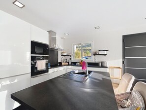 A modern kitchen with white cabinets, a black countertop, a built-in oven, and a window with a view of greenery. - Villa with a pool (Peri)