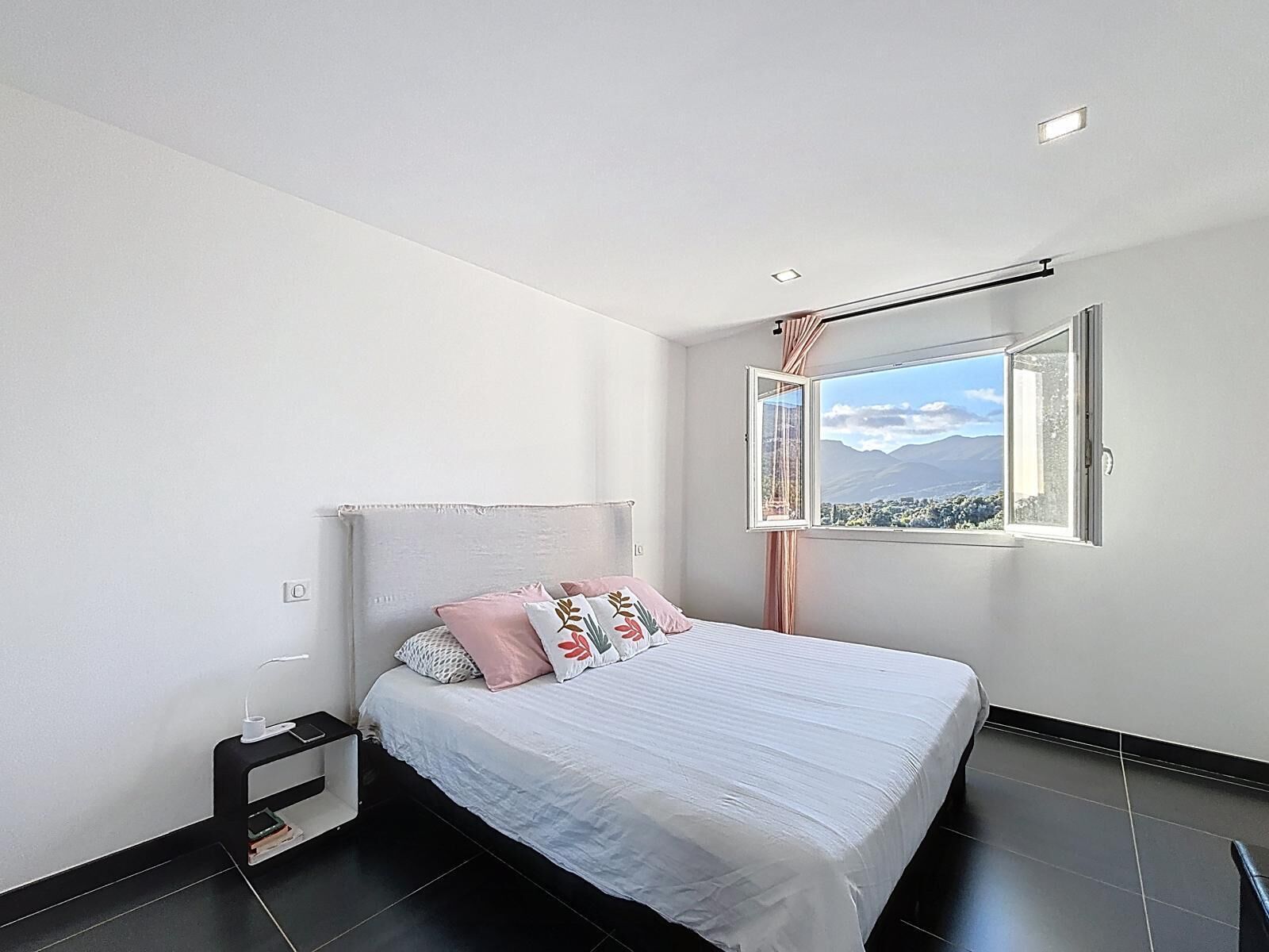 A bedroom with a bed, a nightstand, a window with a view, and a ceiling light.