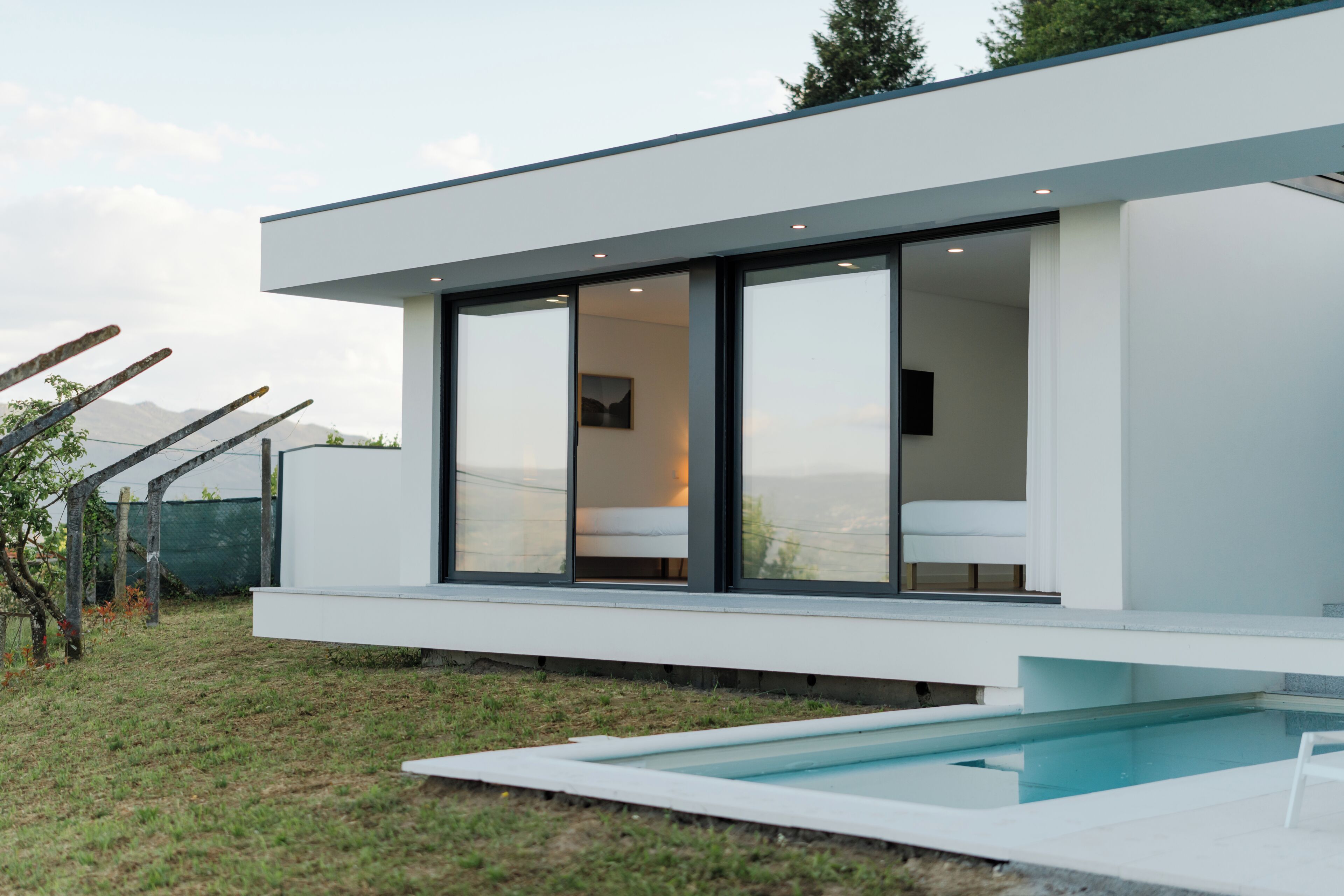 A modern house with a large glass door leading to a bedroom, a swimming pool, and a view of mountains.