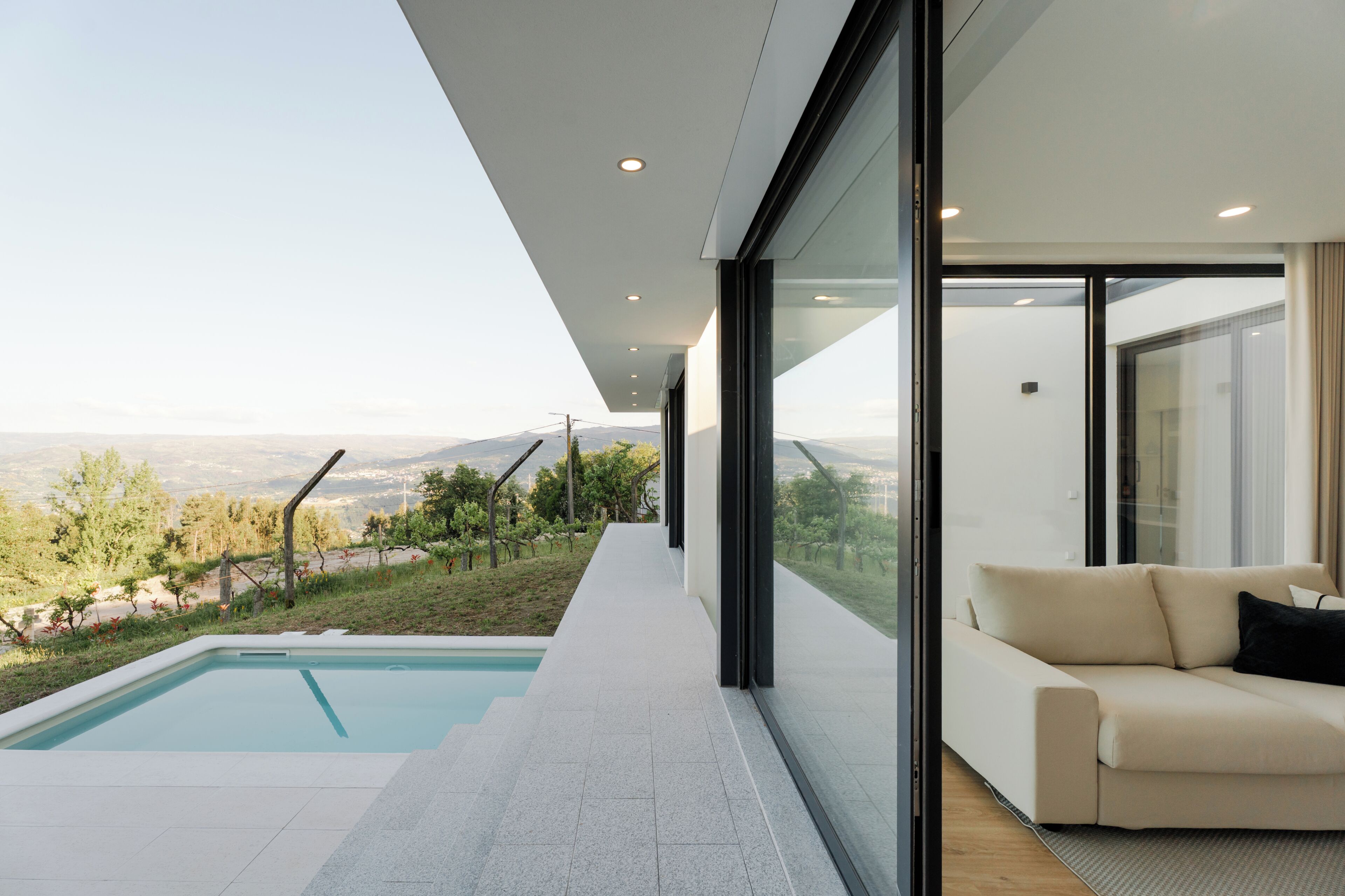 A modern interior with a pool, a sofa, and a view of the landscape.