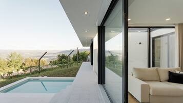 A modern interior with a pool, a sofa, and a view of the landscape.