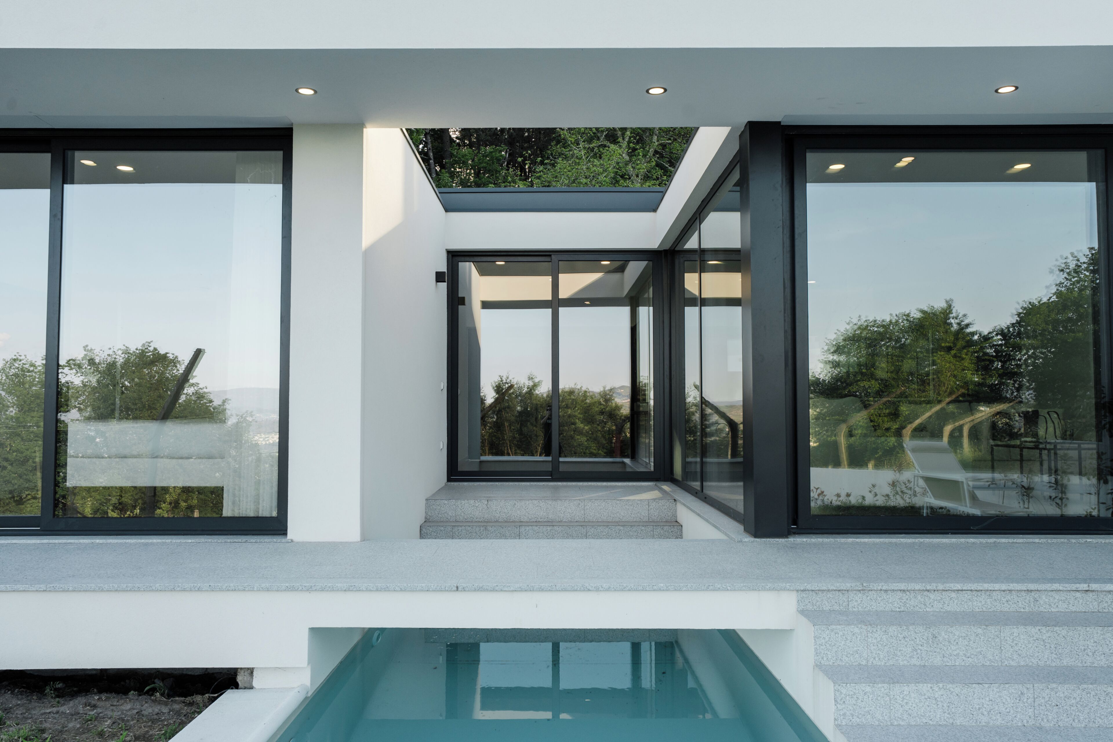 A modern building with large glass windows, a pool, and a staircase leading to an upper level.