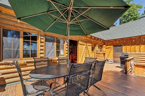 Eine Holzterrasse mit Tisch, Stühlen, einem Sonnenschirm und einem Grill.