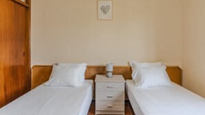 Ein Hotelzimmer mit zwei Einzelbetten, einem Holzschrank, einem kleinen Nachttisch mit Lampe und einer Wanddekoration im Herzen-Design.