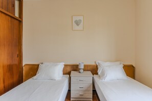 Ein Hotelzimmer mit zwei Einzelbetten, einem Holzschrank, einem kleinen Nachttisch mit Lampe und einer Wanddekoration im Herzen-Design.