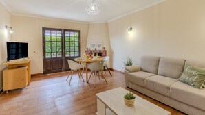 Ein Wohnzimmer mit Sofa, Couchtisch, Fernseher, Essbereich mit Tisch und Stühlen sowie Küchenzeile mit Herd und Schränken.