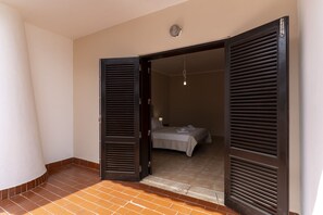 Een open deur die uitkomt op een slaapkamer met een bed, een hanglamp en een zichtbare luchtuitlaat.