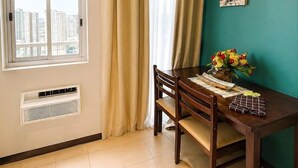 Uma sala de jantar com mesa, cadeiras, janela com cortinas, ar-condicionado na parede e um quadro da Torre Eiffel.