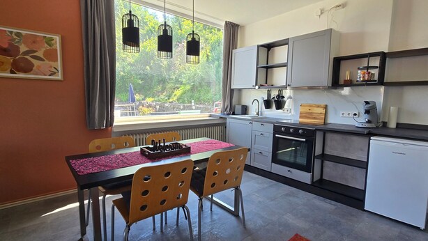 Een compacte keuken met een eetgedeelte, uitzicht door het raam en een klein terras.