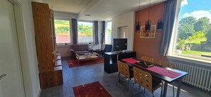 A modern living room with a sofa, a coffee table, a TV, and a dining area with chairs and a table. - Apartment 'FeWo Meyer in Hüddingen' with Private Garden and Wi-Fi (Bad Wildungen)