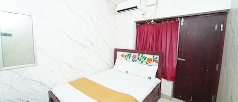 A bedroom with a bed, a wardrobe, a small table, and an air conditioning unit.