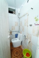 Un baño con inodoro, ducha y un cubo verde.