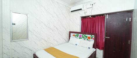 A bedroom with a bed, a ceiling fan, an air conditioning unit, a wardrobe, and a mirror.