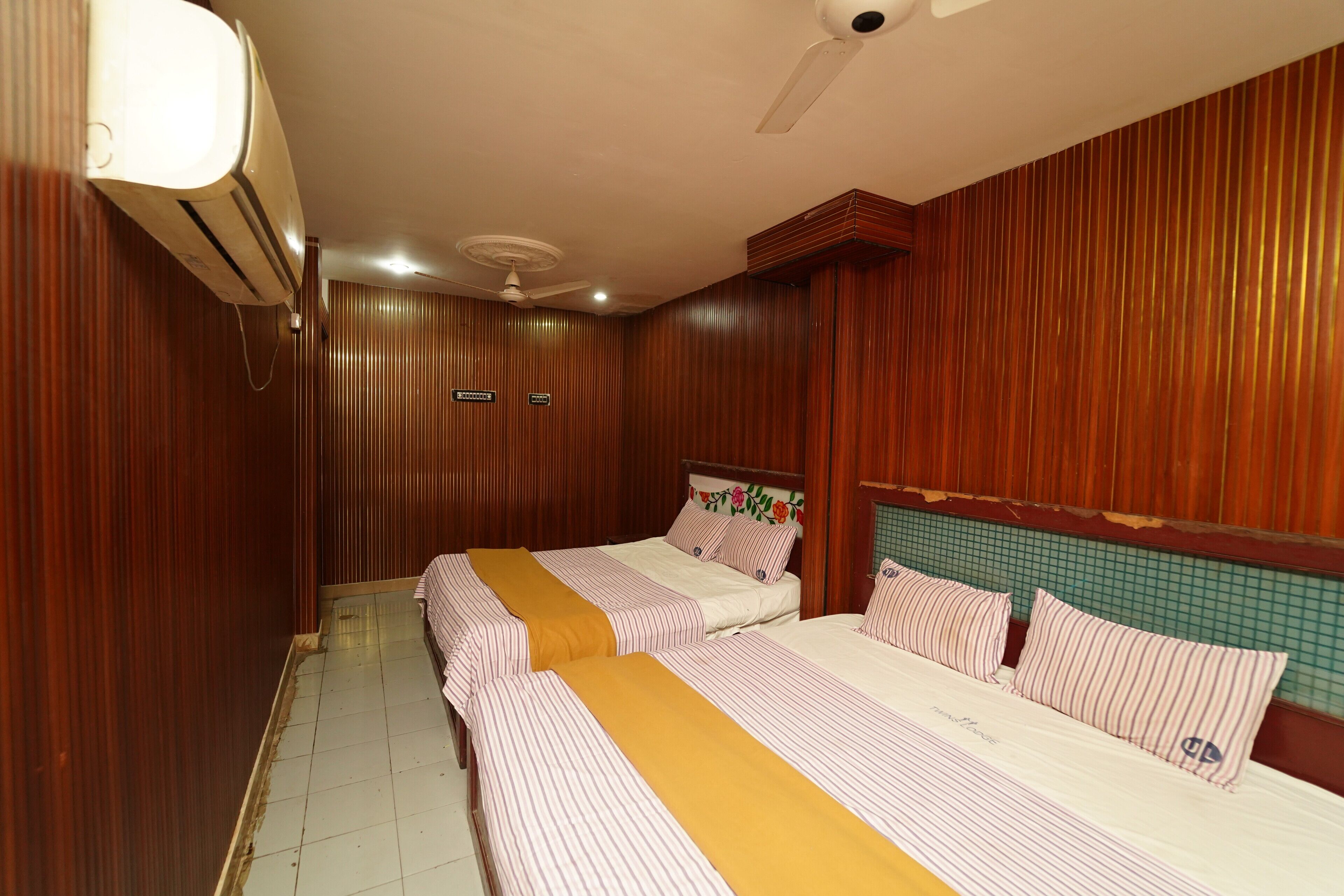 A hotel room with two beds, wooden paneling, a ceiling fan, and an air conditioning unit.