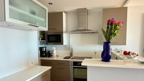 A modern kitchen with a microwave, oven, and a small island with a vase of flowers. - Le Rivage à Pornichet (Pornichet)