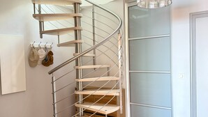 A spiral staircase with metal railings and wooden steps, leading to a room with a glass door and a hanging light fixture. - Le Rivage à Pornichet (Pornichet)
