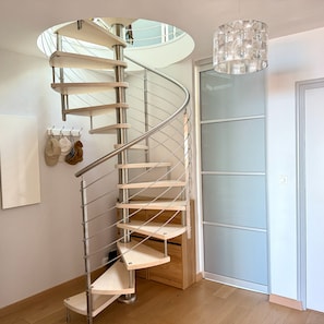 Eine Wendeltreppe mit Metallgeländern und Holzstufen führt zu einem Raum mit Glastür und einer hängenden Leuchte.