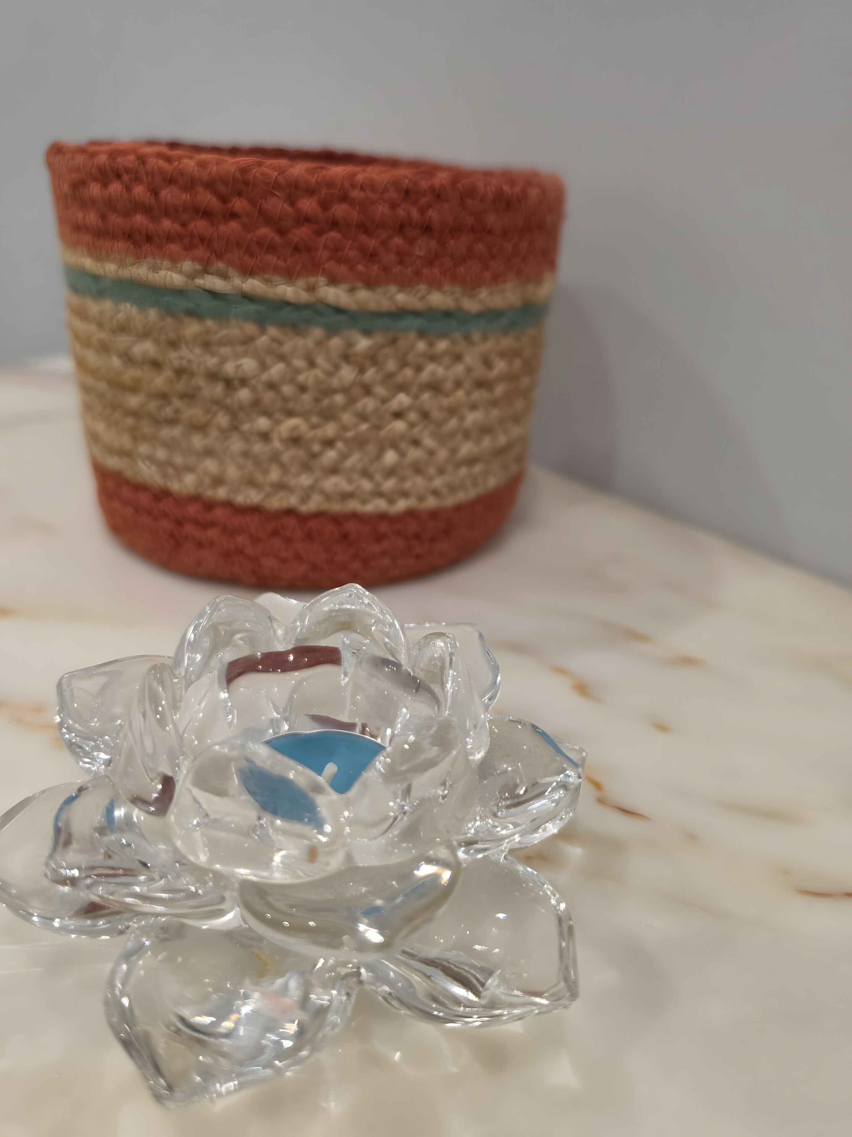 Een gehaakte houder met een gestreept patroon en een glazen object met een blauw midden.