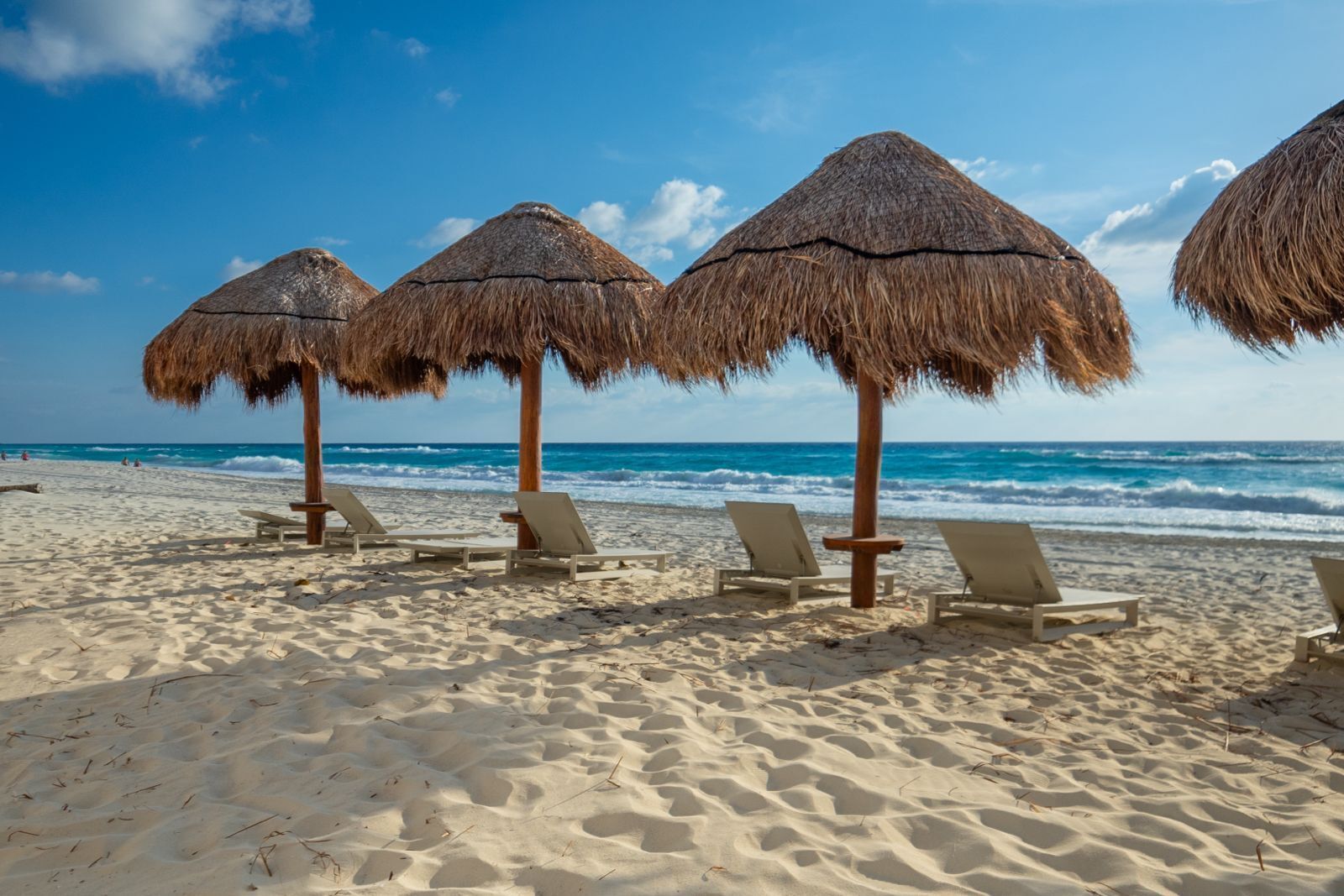 Una playa con sombrillas de paja y sillas reclinables.