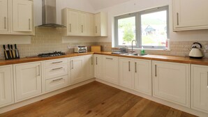 A kitchen with white cabinets, a wooden countertop, a gas stove, a toaster, and a window with a view of the outside. - Craigard (Aberfeldy)
