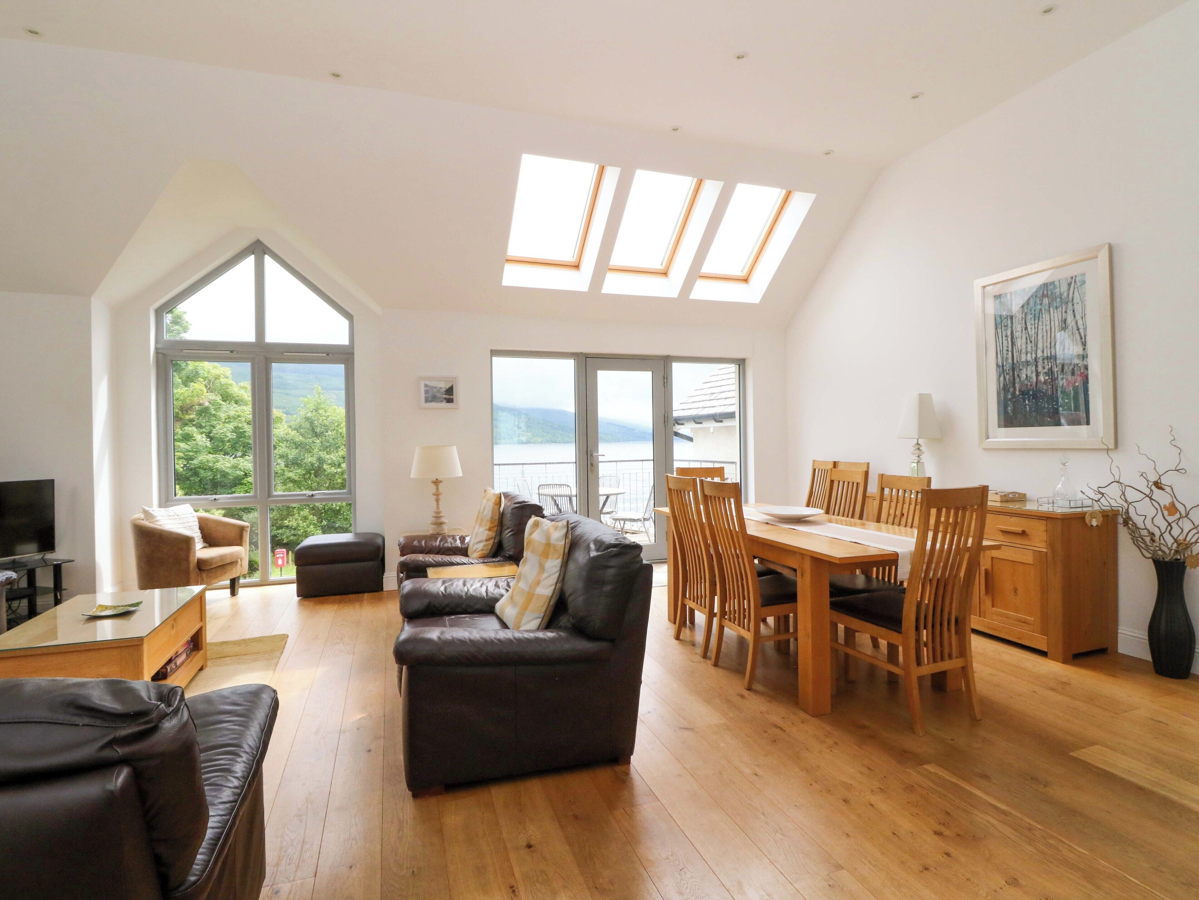 A spacious living area with a high ceiling, large windows, a dining table, and a cozy seating arrangement.