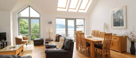 A spacious living area with a high ceiling, large windows, a dining table, and a cozy seating arrangement.