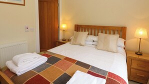A hotel room with a bed, two bedside tables, a wooden door, and a radiator. - Craigard (Aberfeldy)