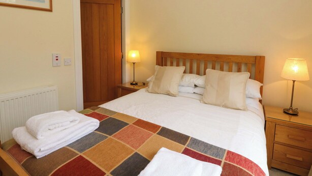 A hotel room with a bed, two bedside tables, a wooden door, and a radiator. - Craigard (Aberfeldy)