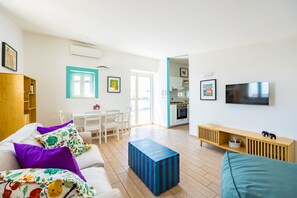 A modern living room with a sofa, a coffee table, and a TV. There is a kitchen in the background with a dining area. - Viewsuvio Two Apartments & Terraces (Naples)