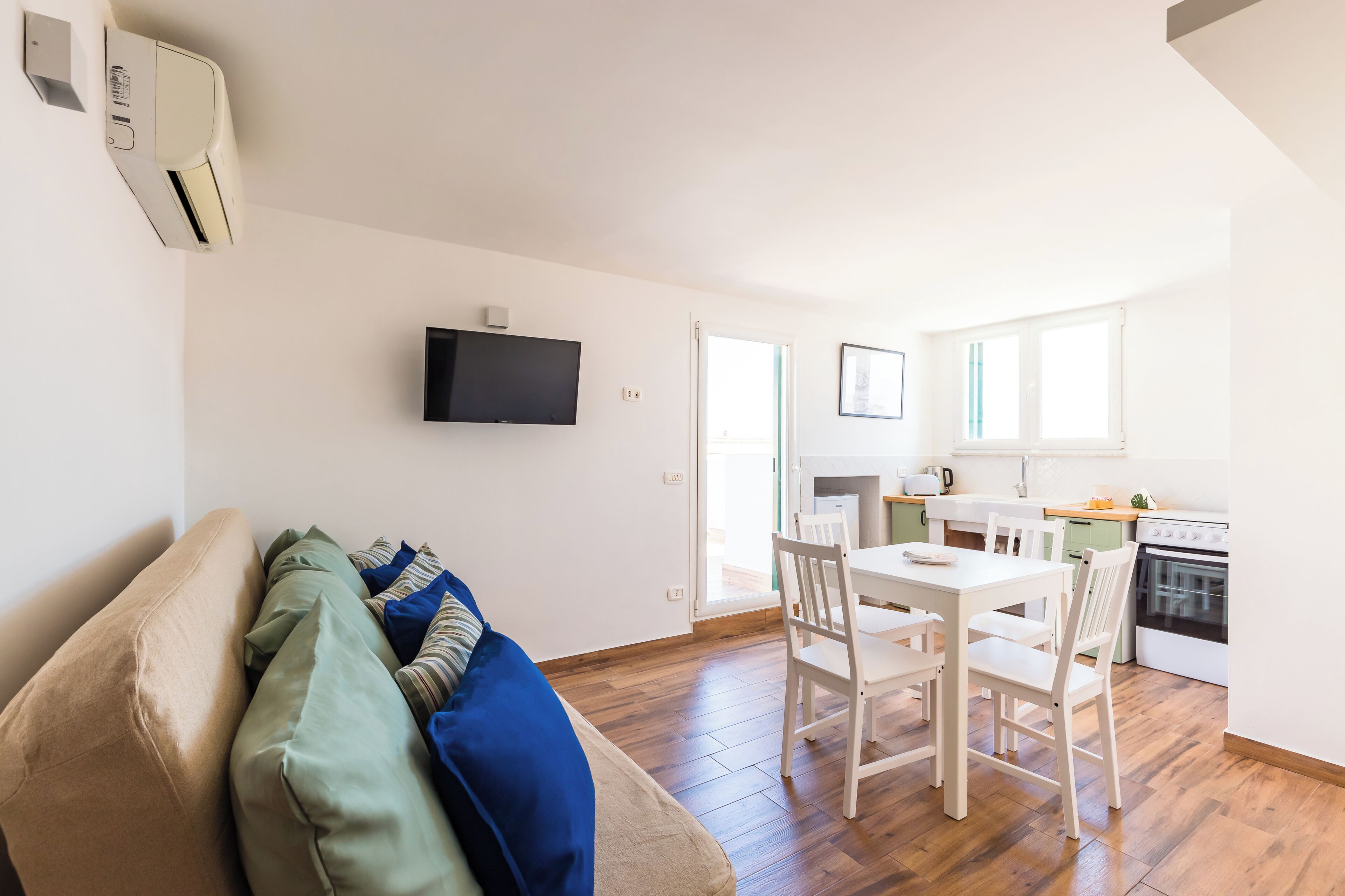 Un salon moderne comprenant un canapé, une table à manger avec des chaises, un coin cuisine avec une cuisinière et un téléviseur à écran plat fixé au mur.