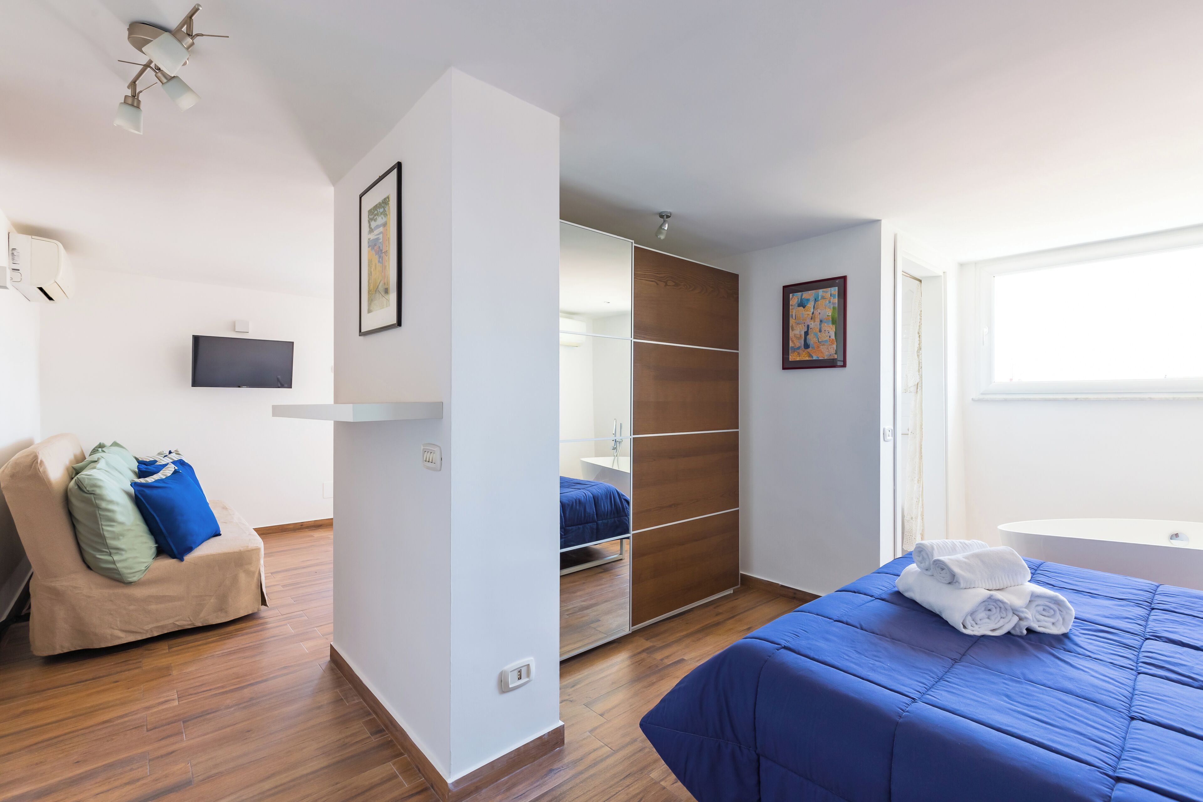 A bedroom with a bed, a chair, a wardrobe, a television, and a bathroom.