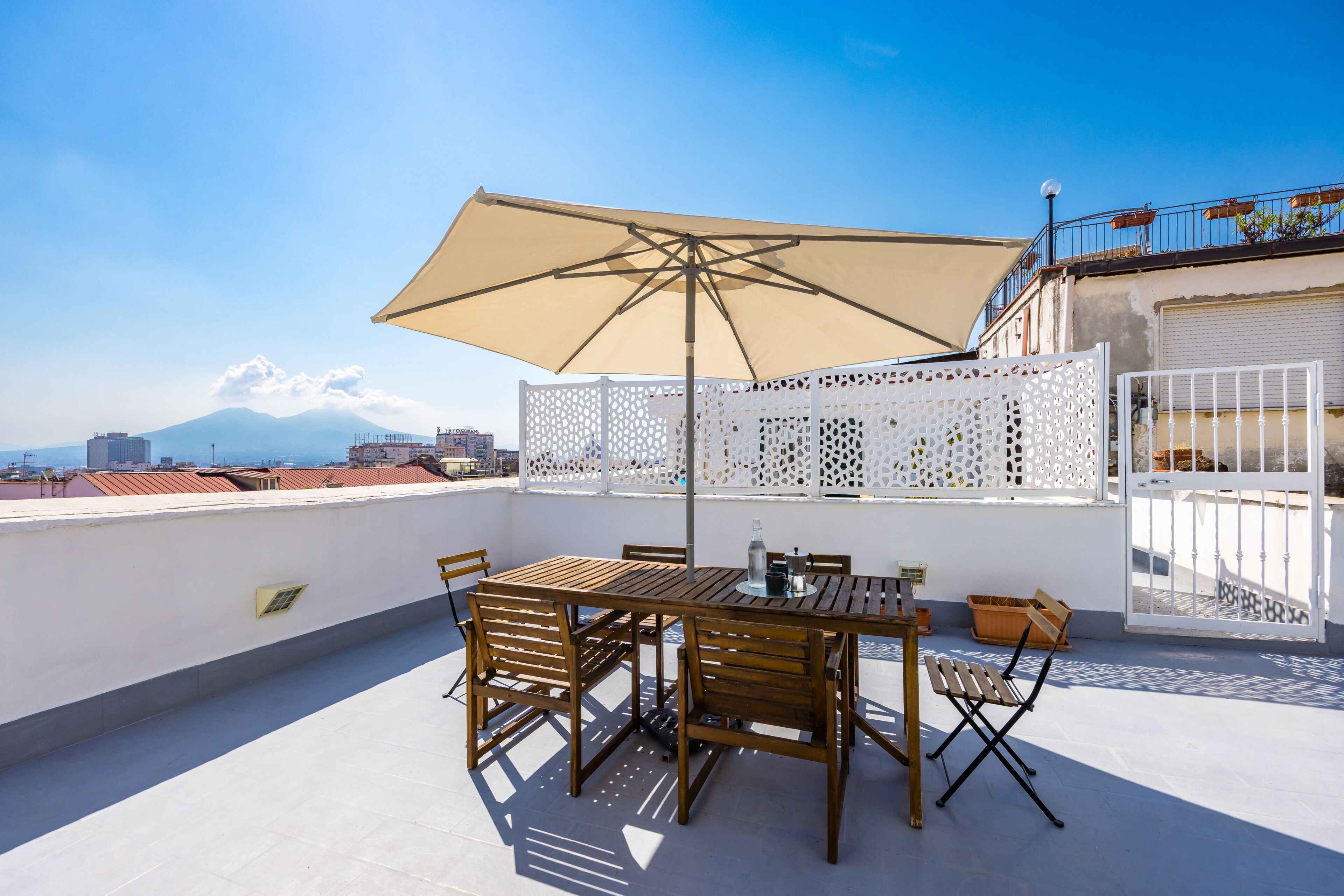 A rooftop terrace with a table and chairs, a large umbrella, and a white decorative fence.