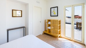 A bedroom with a bed, a wooden shelf with towels, a framed picture, and a sliding glass door leading to an outdoor area. - Viewsuvio Two Apartments & Terraces (Naples)